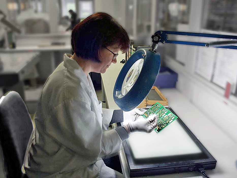 Mitarbeiterin bei der optischen Kontrolle einer Leiterplatte unter der Lupenleuchte